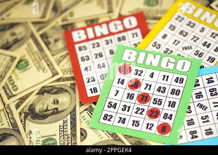 Many bingo boards or playing cards for winning chips and big amount of dollar bills. Classic american or canadian five to five bingo cards on money Stock Photo