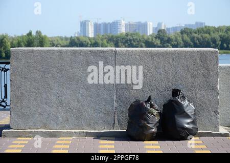 Two black garbage bags on tiled street floor at concrete fence in city Stock Photo