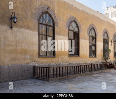 Wooden arched window with wrought iron grid over yellow stone bricks wall and wooden balustrade Stock Photo