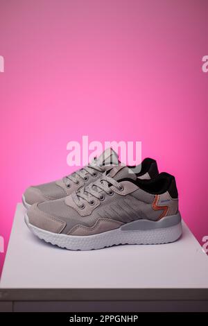 Pair of sports shoes standing on white podium on pink background. Stock Photo