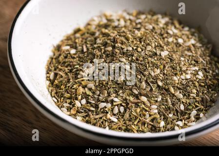 Mixed zaatar or zatar spices in white bowl close up. Oriental herbal seasoning zaatar or zattar. Arabic cuisine. Stock Photo