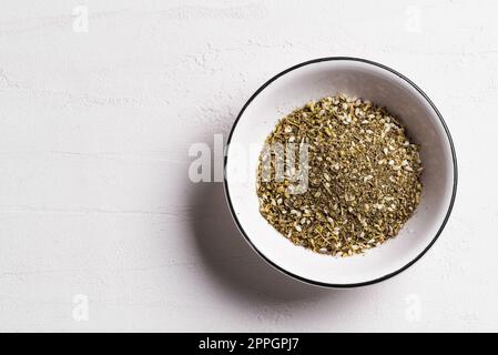 Mixed zaatar or zatar spices in white bowl on white background, copy space. Oriental herbal seasoning zaatar or zattar. Arabic cuisine. Stock Photo