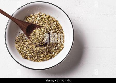 Mixed zaatar or zatar spices in white bowl on white background, copy space. Oriental herbal seasoning zaatar or zattar. Arabic cuisine. Stock Photo