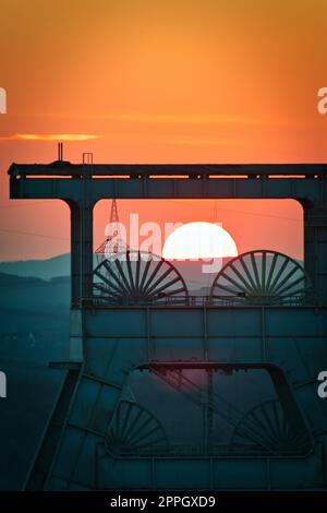 Vertical shot of a headframe tower with a golden sun setting in the background in Herten, Germany Stock Photo