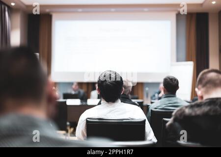 Business and entrepreneurship symposium. Speaker giving a talk at business meeting. Audience in the conference hall. Rear view of unrecognized participant in audience Stock Photo