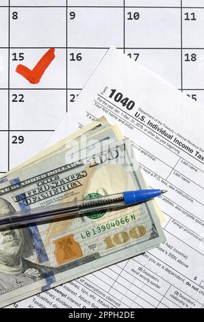 1040 Individual Income Tax Return blank with dollar bills, calculator and pen on calendar page with marked 15th April Stock Photo