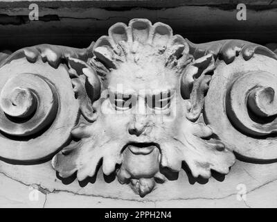 Decorative detail on the facade. Relief on the facade of a building. Stucco molding in the form of a man's head with curly hair, mustache and curls on the sides. High relief concrete bas-relief. Stock Photo