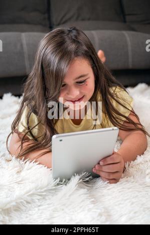 Adorable little girl using a digital tablet on the floor at home. Stock Photo