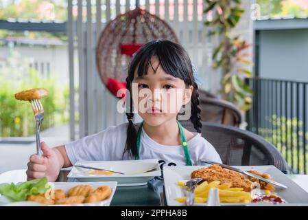 Asian young girl Eating Chicken nuggets fast food on table. Stock Photo