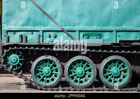 Side view of the vehicle on a caterpillar track with black tracks and green wheels and a side metal wall Stock Photo