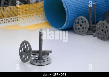 A set of construction items for the insulation of walls. Plastic dowels, a roll of mesh for the insulation of facades and a corner profile with a grid lie on the foam polystyrene surface Stock Photo