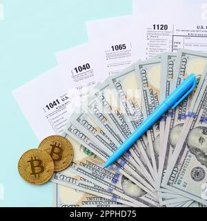 Bitcoins lies with the tax forms and hundred dollar bills on a light blue background. Income tax return Stock Photo