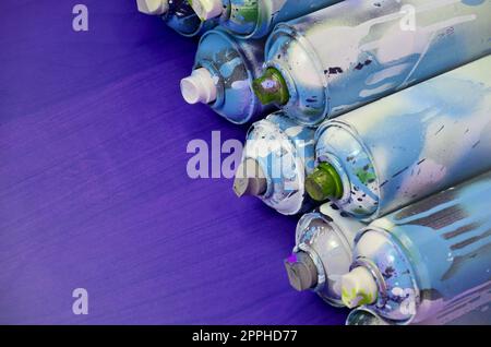 Still life with a large number of used colorful spray cans of aerosol paint lying on the treated wooden surface in the artist's graffiti workshop. Dirty and stained cans for spray art Stock Photo