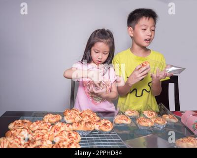Adorable kid girl and boy separate packing baked pork sausage with mayonnaise bread,  domestic kitchen, Child  helping his parents Stock Photo