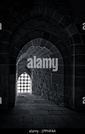 Stone wall with a backlit window with iron grid at an old citadel in Alexandria, Egypt Stock Photo