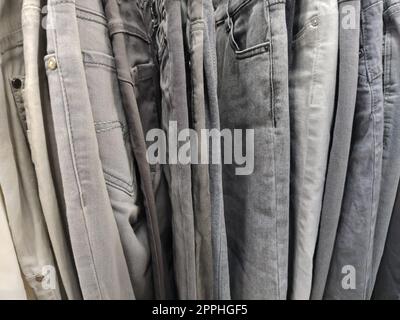 Clothes hung on hangers. Assortment of second hand store. Clothing hanging on a rack, ready for sale to customers. Saving money in crisis. Cheap shopping. Jeans and pants. Stock Photo