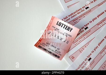 Red lottery ticket lies on pink gambling sheets with numbers for marking to play lottery. Lottery playing concept or gambling addiction. Close up Stock Photo