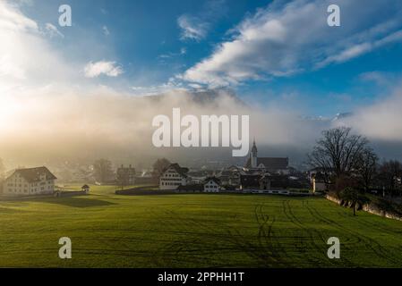 Morning haze or evening haze with the light rays of the sun penetrating it in the town of Schwyz in Switzerland Stock Photo