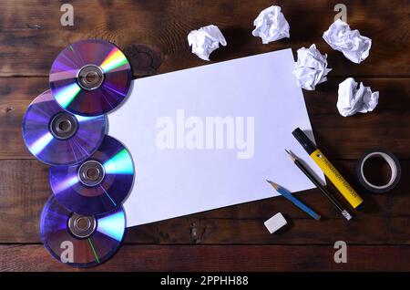 A school or office still life with a white blank sheet of paper and many office supplies. The school supplies lie on a brown wooden background. Place for text Stock Photo