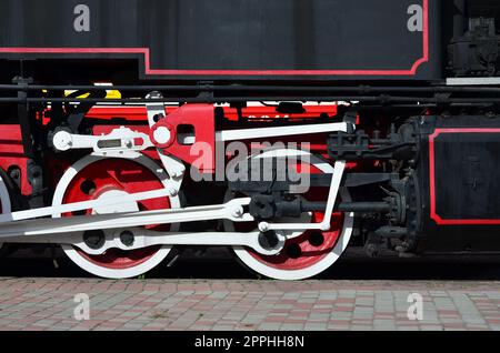 Wheels of the old black steam locomotive of Soviet times. The side of the locomotive with elements of the rotating technology of old trains Stock Photo