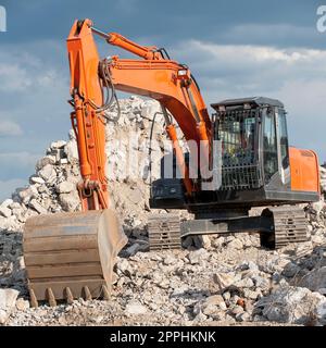 Square photo of an excavator with chain wheels and shovel standing on a pile of rubble without logos and other legal identifiers. Stock Photo