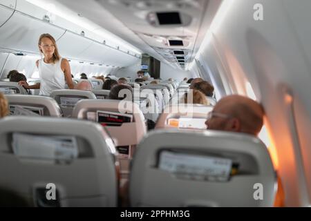 Pretty, young happy woman aboard an airplaneduring a lang haul commercial flight - stretching her legs a bit, walking in the aisle Stock Photo