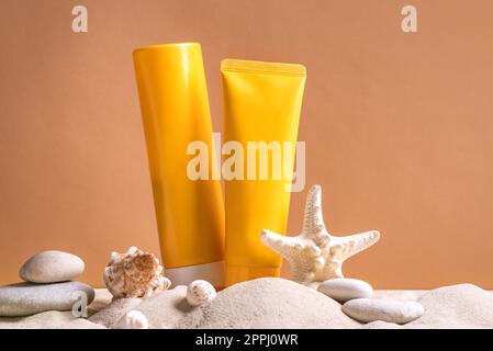 Sunblock in orange cosmetic tubes on beach sand and beige background, side view. Summer vacation and skin care concept with starfish and sea shells, s Stock Photo