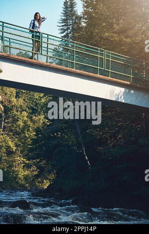 The perfect day to spend in nature. an attractive young woman standing on a bridge surrounded by nature. Stock Photo
