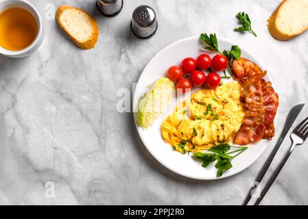 Breakfast with scrambled eggs, fried bacon and vegetables, top view, copy space. Stock Photo