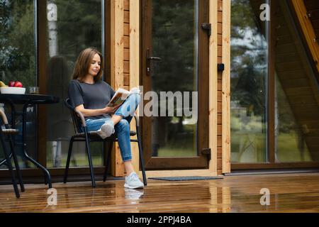Cute woman sits on terrace and reads novel Stock Photo