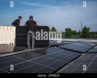 Male team engineers installing stand-alone solar photovoltaic panel system. Electricians mounting blue solar module on roof of modern house. Alternative energy concept Stock Photo