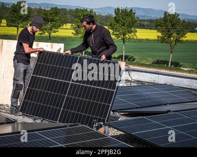 Male team engineers installing stand-alone solar photovoltaic panel system. Electricians mounting blue solar module on roof of modern house. Alternative energy concept Stock Photo