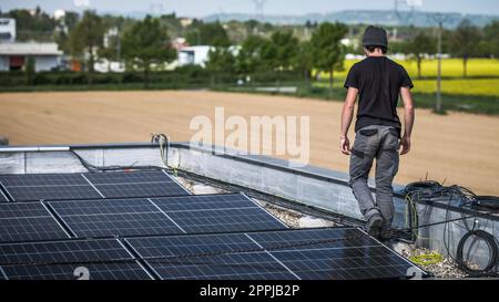 Male team engineers installing stand-alone solar photovoltaic panel system. Electricians mounting blue solar module on roof of modern house. Alternative energy concept Stock Photo