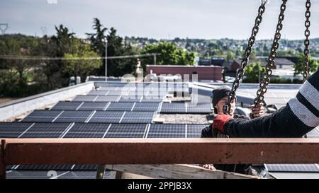 Male team engineers installing stand-alone solar photovoltaic panel system. Electricians mounting blue solar module on roof of company roof. Alternative energy concept Stock Photo