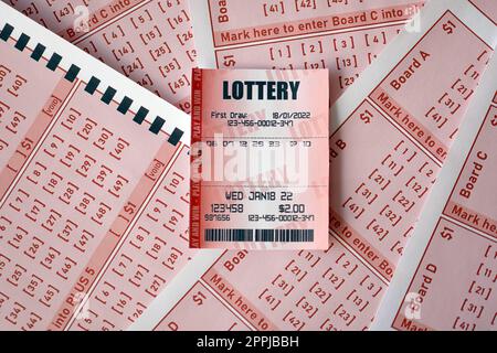 Red lottery ticket lies on pink gambling sheets with numbers for marking to play lottery. Lottery playing concept or gambling addiction. Close up Stock Photo