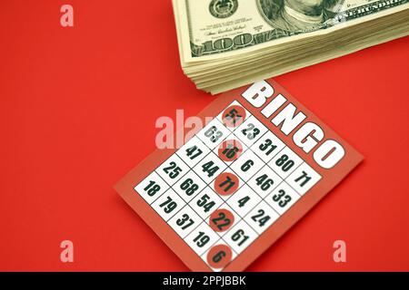 Red bingo board or playing card for winning chips and stack of dollar bills. Classic american or canadian five to five bingo card on red background Stock Photo