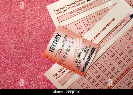 Red lottery ticket lies on pink gambling sheets with numbers for marking to play lottery. Lottery playing concept or gambling addiction. Close up Stock Photo