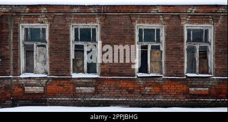 An old brick wall of an apartment house with a lot of boarded up windows without glass Stock Photo