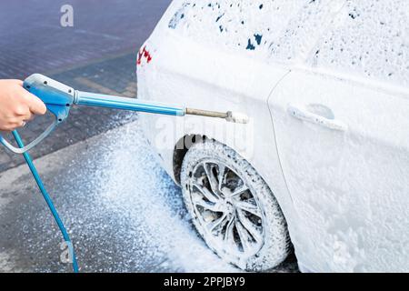 Hand washing with high pressure water in a car wash outside. A jet of foam. The concept of hand washing, self-service. Stock Photo