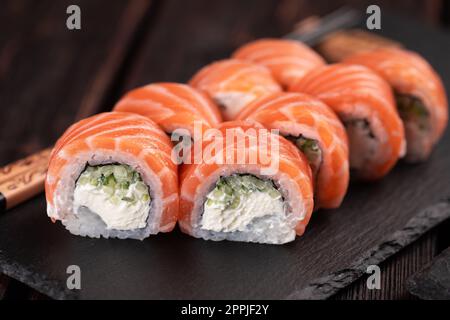 Sushi roll philadelphia with salmon and cucumber and cream cheese on black background close-up. Sushi menu. Japanese food concept Stock Photo