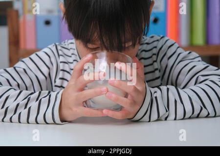 Cute Asian girl drinking a glass of milk at home in living room. Little girl drinking milk in the morning before going to school. Healthy food in chil Stock Photo