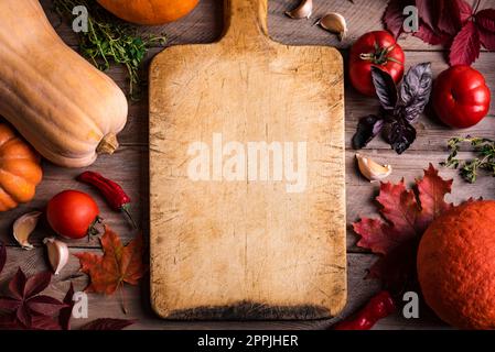 Autumn cooking background: empty rustic cutting board and seasonal pumpkins, vegetables and herbs, cooking ingredients. Seasonal organic healthy food Stock Photo