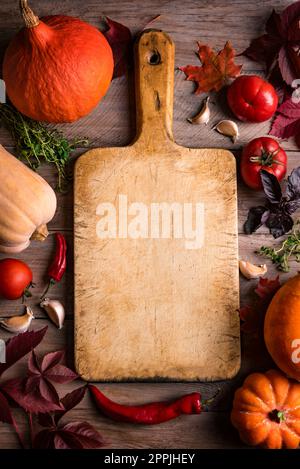 Autumn cooking background: empty rustic cutting board and seasonal pumpkins, vegetables and herbs, cooking ingredients. Seasonal organic healthy food Stock Photo