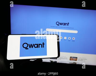 Person holding smartphone with logo of French search engine company Qwant SAS on screen in front of website. Focus on phone display. Stock Photo