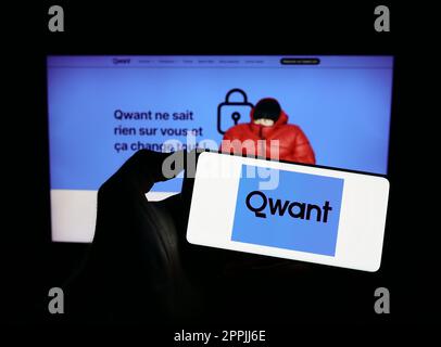 Person holding mobile phone with logo of French search engine company Qwant SAS on screen in front of business web page. Focus on phone display. Stock Photo