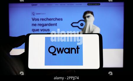 Person holding cellphone with logo of French search engine company Qwant SAS on screen in front of business webpage. Focus on phone display. Stock Photo