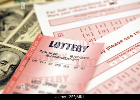 Red lottery ticket lies on pink gambling sheets with numbers for marking on big amount of hundred dollar bills. Lottery playing concept or gambling addiction. Close up Stock Photo