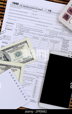 Composition of items lying on the 1040 tax form. Dollar bills, calculator, smartphone, paper clip and notepad. The time to pay taxes Stock Photo