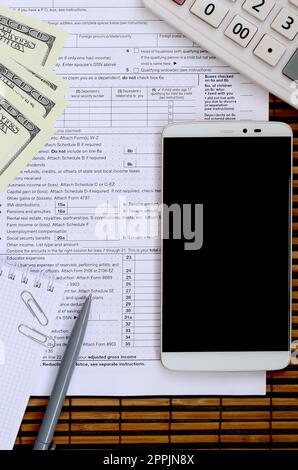 Composition of items lying on the 1040 tax form. Dollar bills, pen, calculator, smartphone, paper clip and notepad. The time to pay taxes Stock Photo