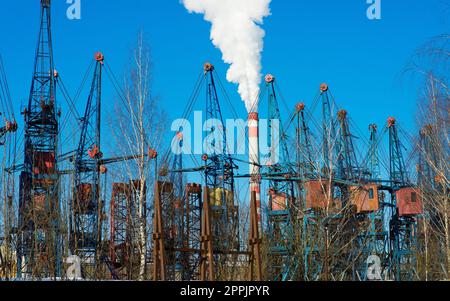 Industrial landscape, cranes, pipes with smoke. Air pollution from smokestacks, ecological problems. Stock Photo